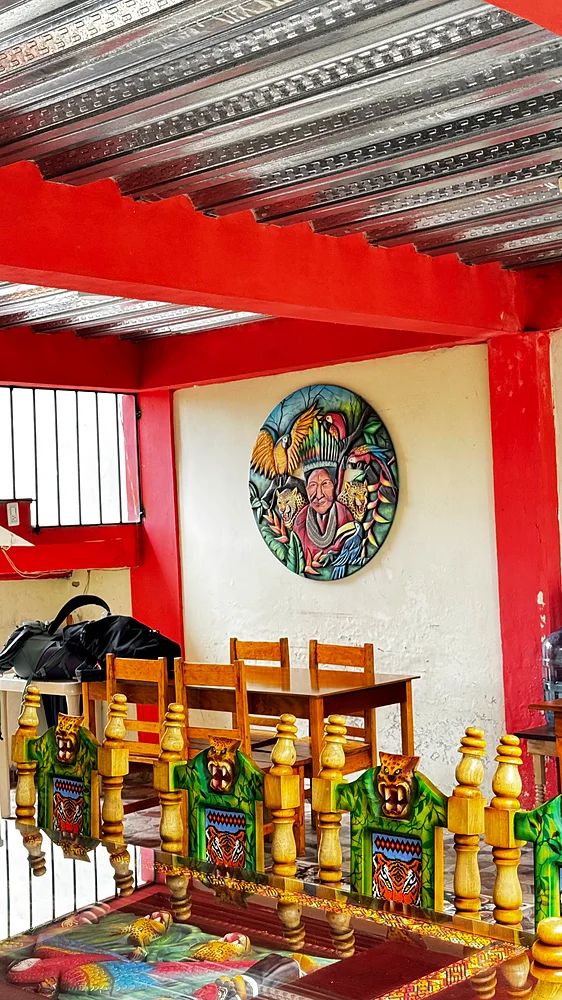 Common room with hand-carved Kamentsá chairs and a carved wall relief at Shanayoy, Colombia
